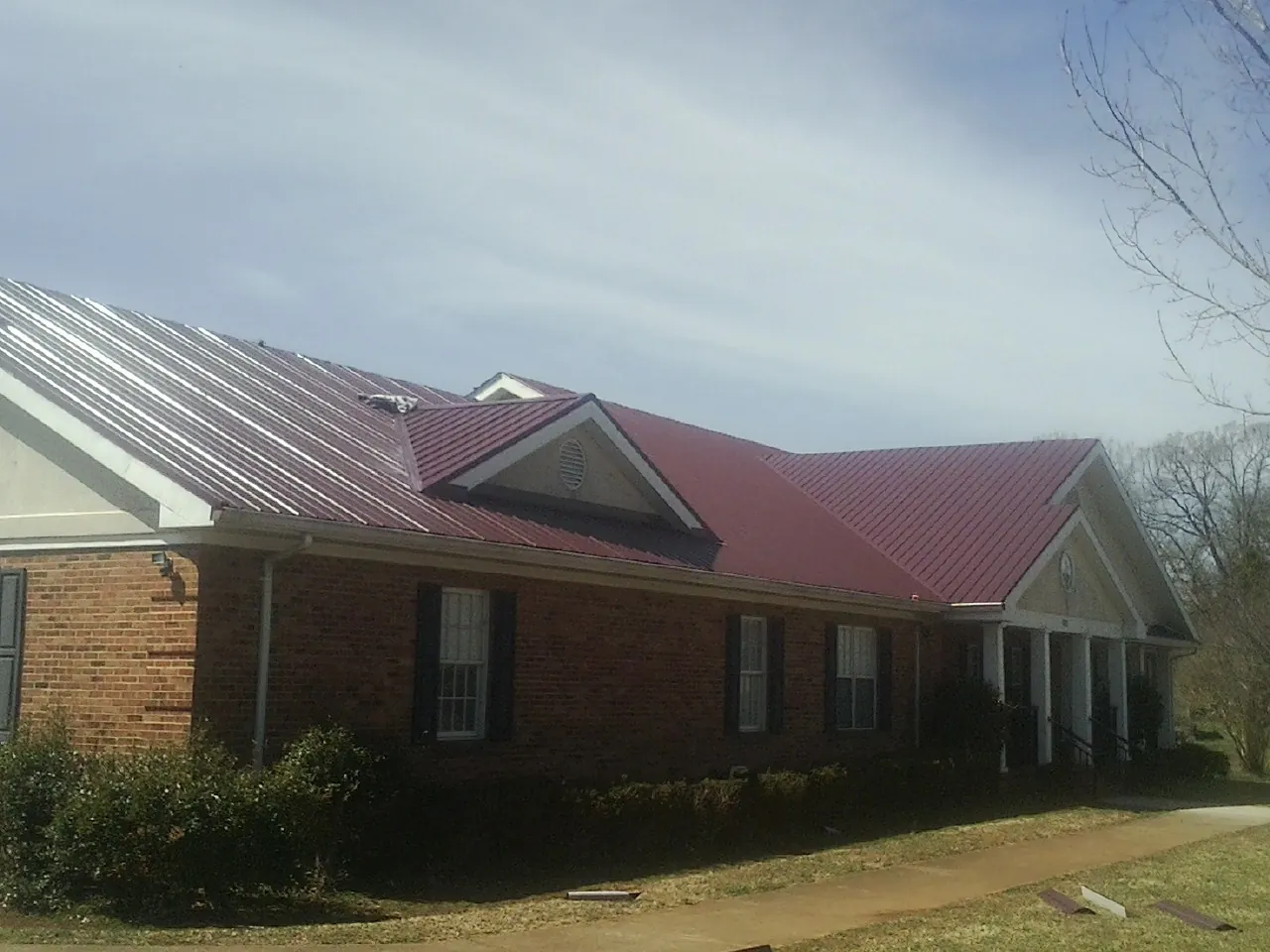 Red metal roof with gabled entries on a long brick building, from a Hail Damage Roof Repair job in Oracle