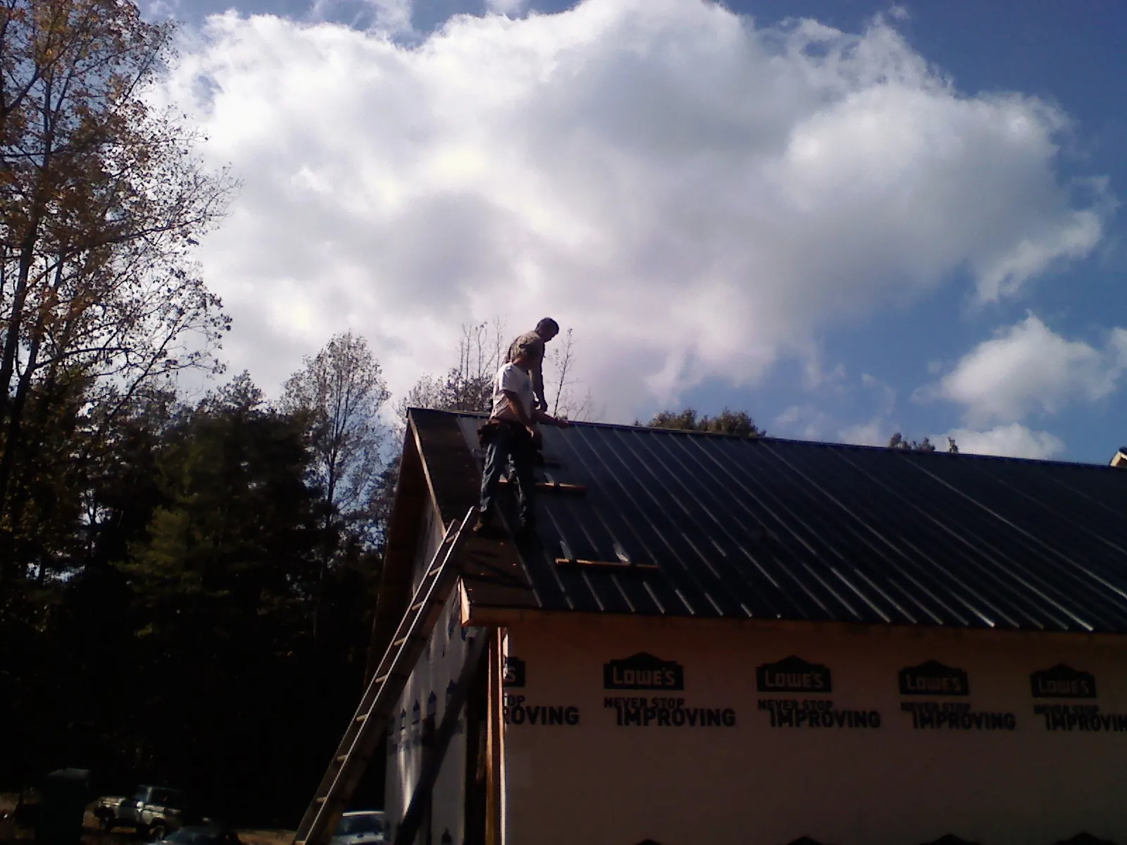 Roofer fastening dark metal panels high against a cloudy sky, from a Roof Inspection job in Oracle